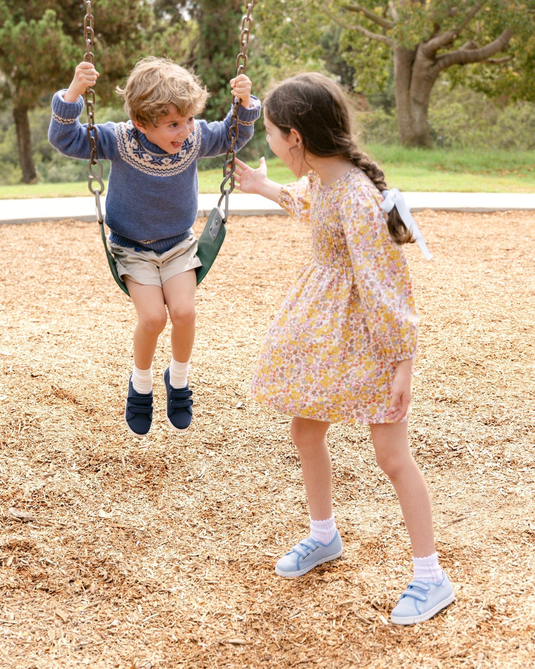 Two children playing on a swing set in a park.