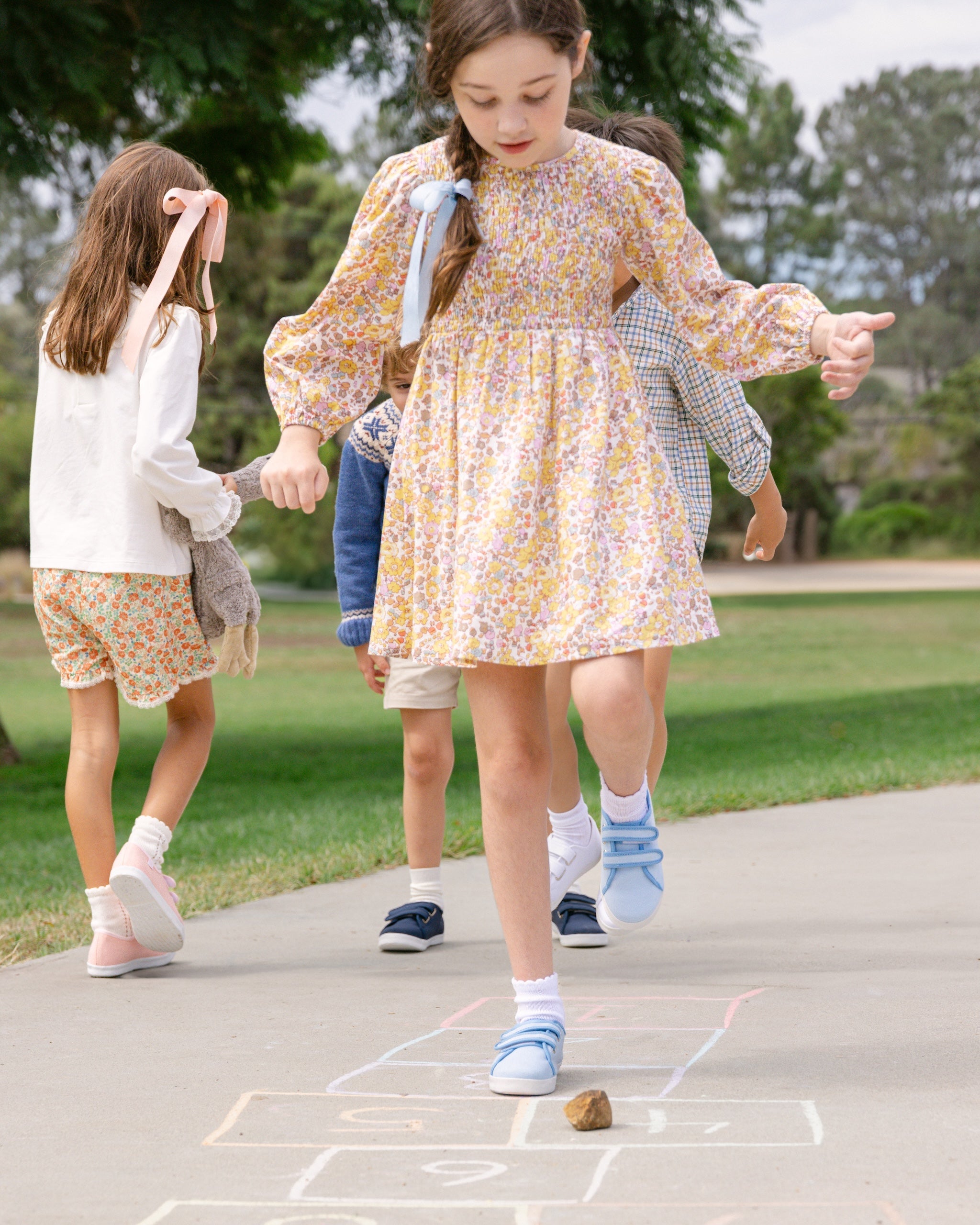 Two children playing hopscotch on a sidewalk with trees in the background