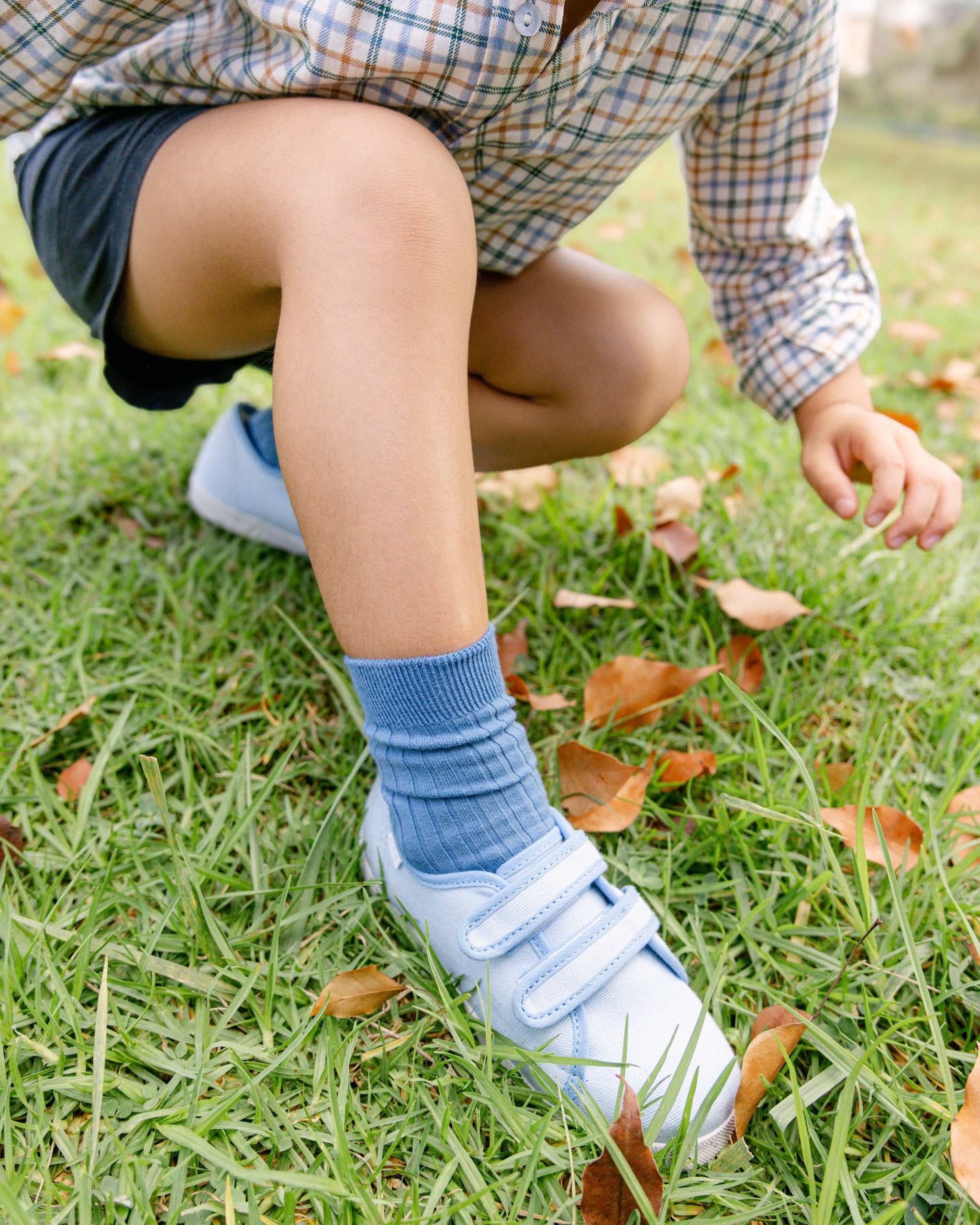 Person wearing blue socks and white sneakers on grass with fallen leaves