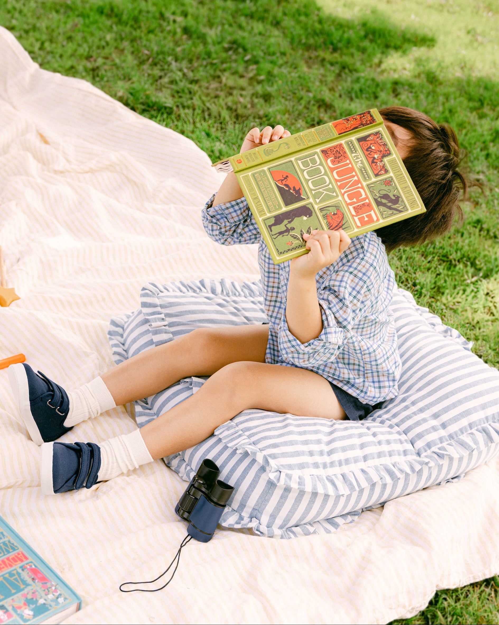 Person lying on a blanket outdoors, holding a book